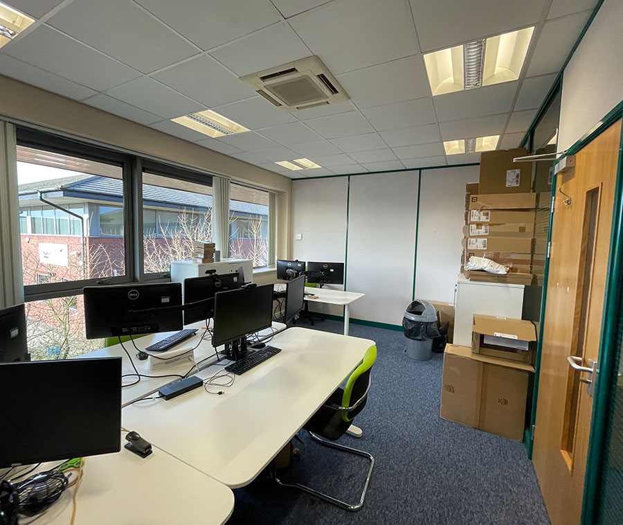 Interior of an office, featuring laptops and desks.